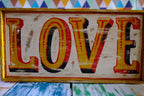 Rustic wooden hand painted  fairground style sign with 'LOVE' in colorful letters on geometric background