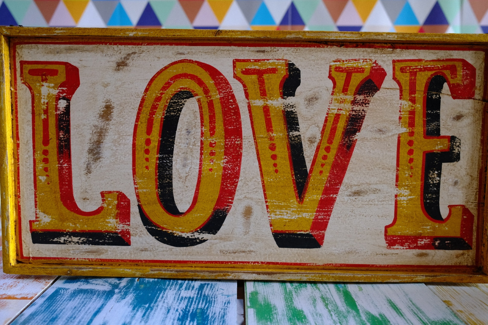 Rustic wooden hand painted  fairground style sign with 'LOVE' in colorful letters on geometric background