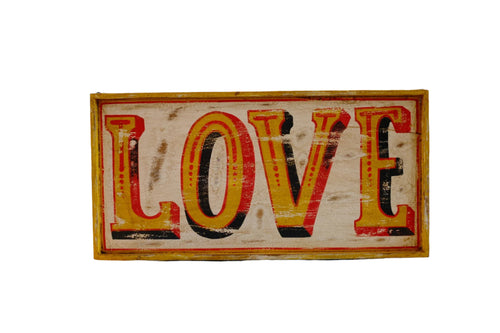 Wooden sign with 'LOVE' in colorful letters against a geometric patterned wall.