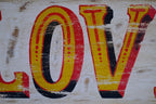 Close-up of a distressed 'LOVE' sign with yellow and red letters on a textured background.