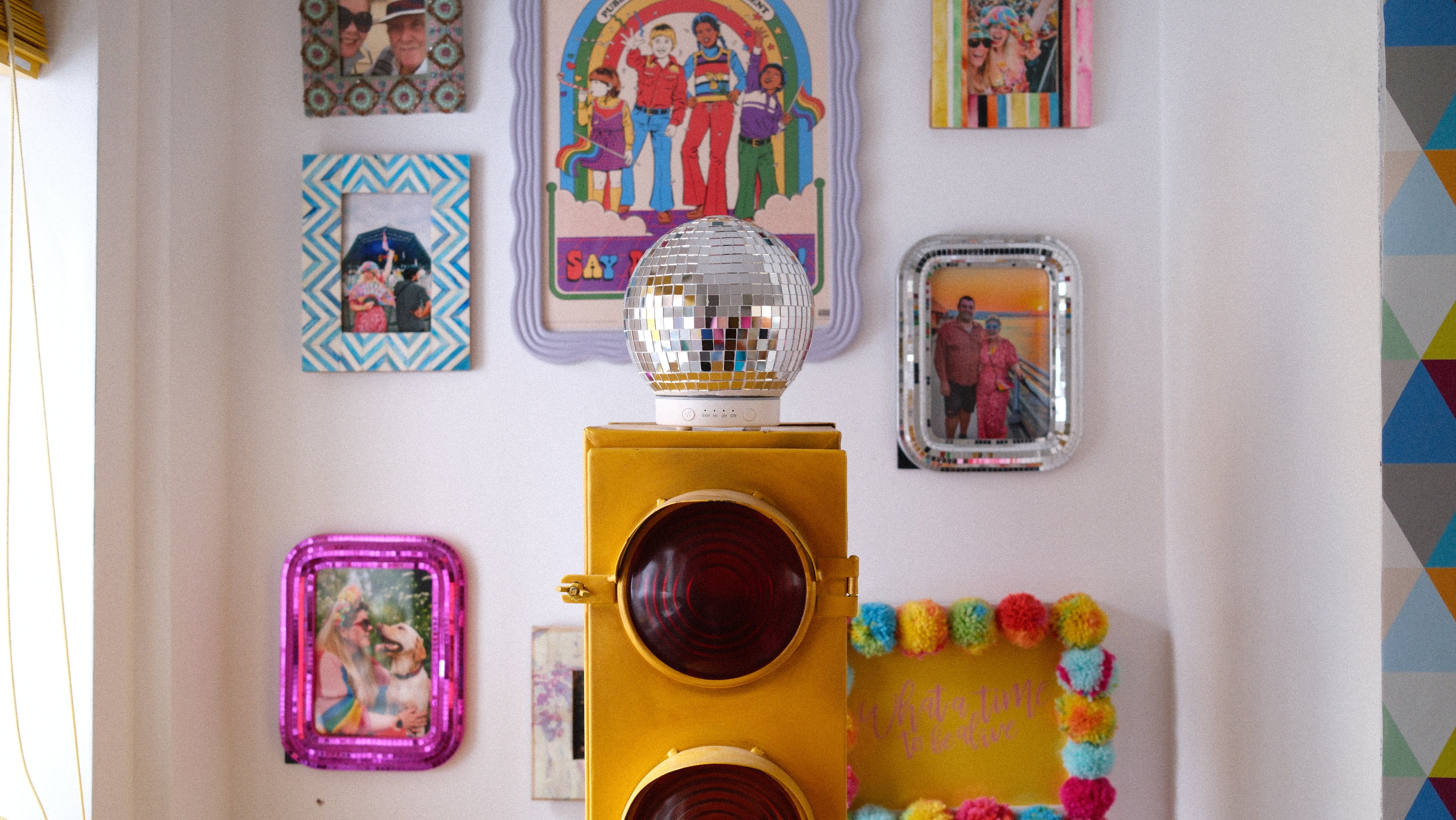 Colorful wall decor with disco ball diffuser and various framed pictures on a white wall.