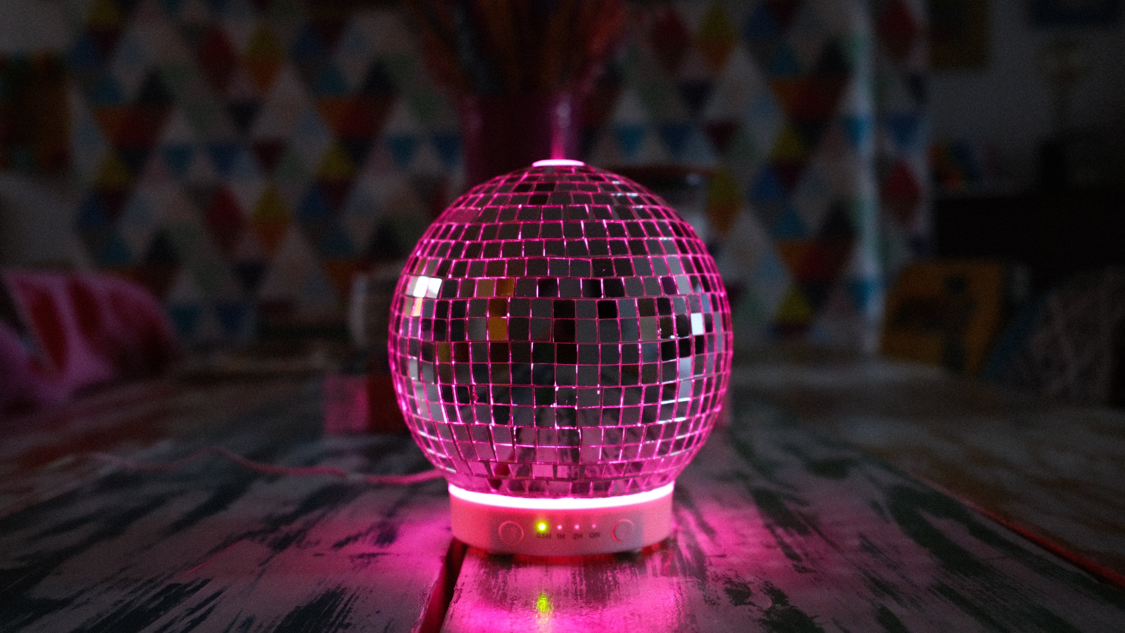 Pink disco ball on a table with a colorful patterned curtain in the background