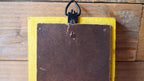 Yellow card holder with a brown leather patch on a wooden surface