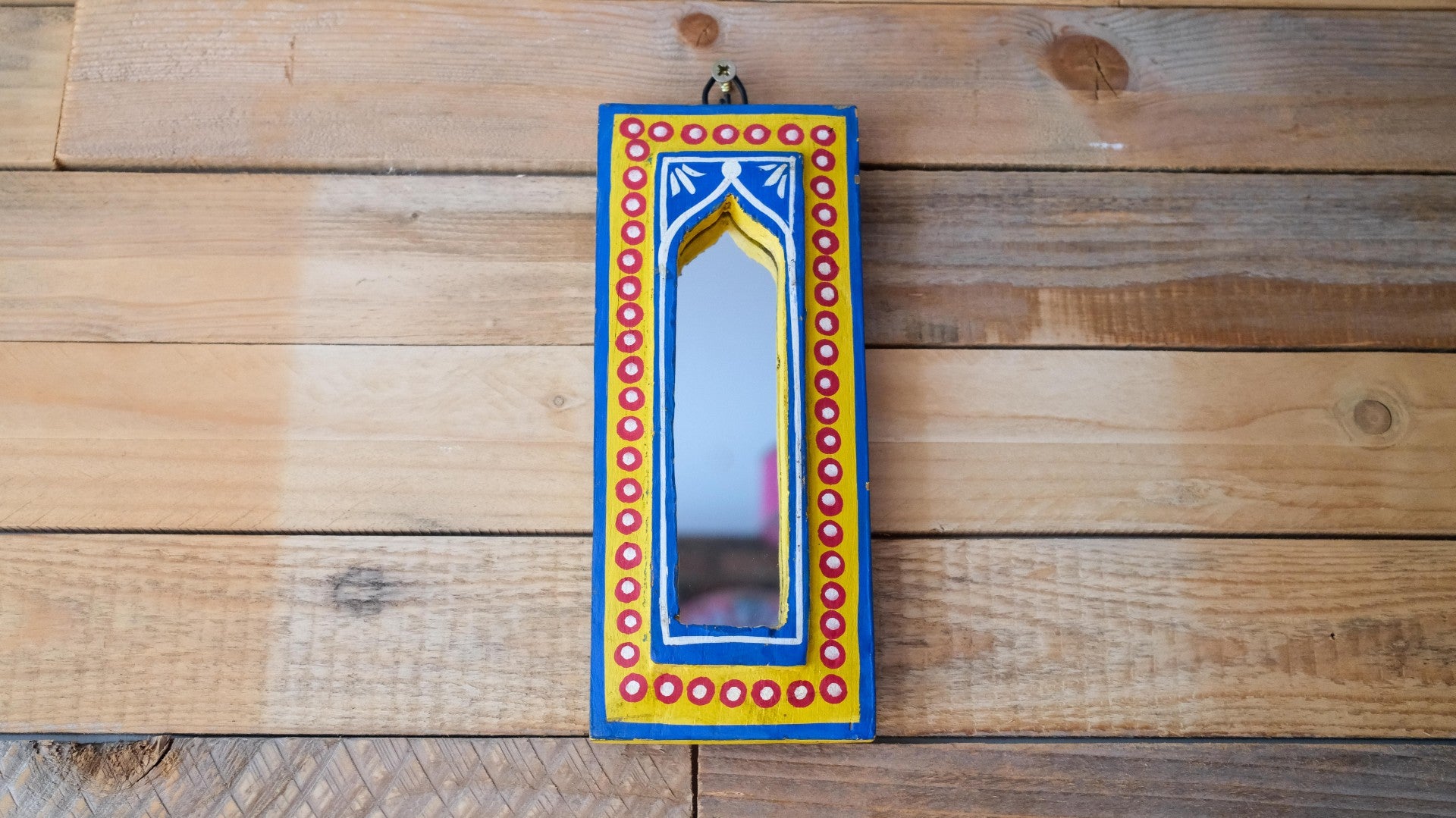 Decorative mirror with a colorful frame on a wooden wall