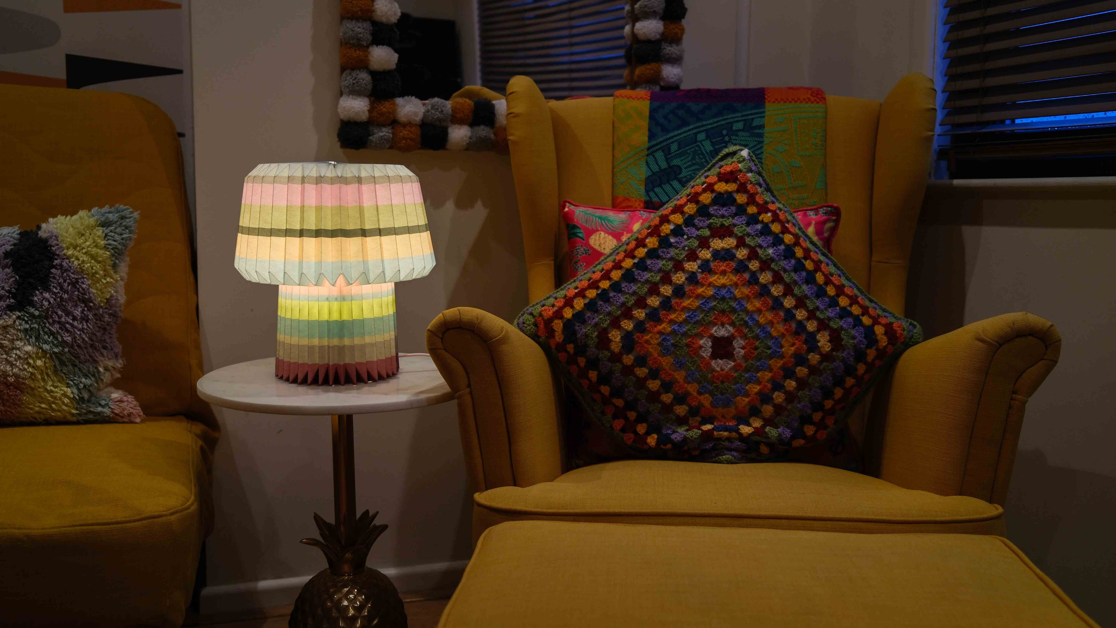 Yellow armchair with colorful cushions and a patterned lamp in a cozy room.