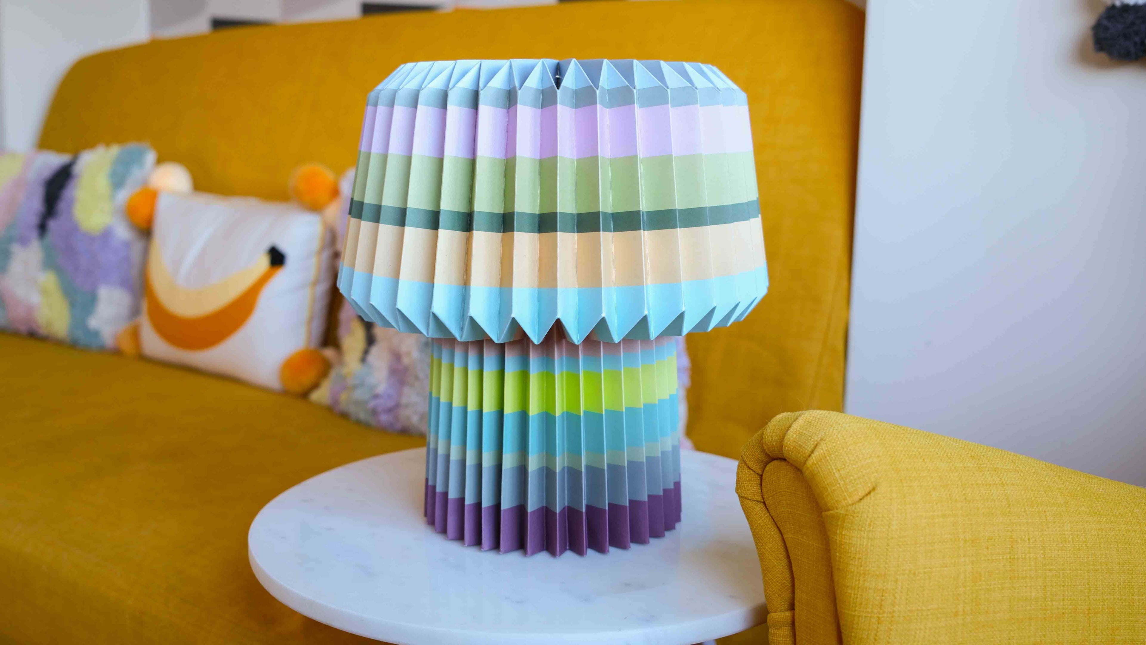 Colorful origami-style lamp on a white surface with a yellow couch and pillows in the background.