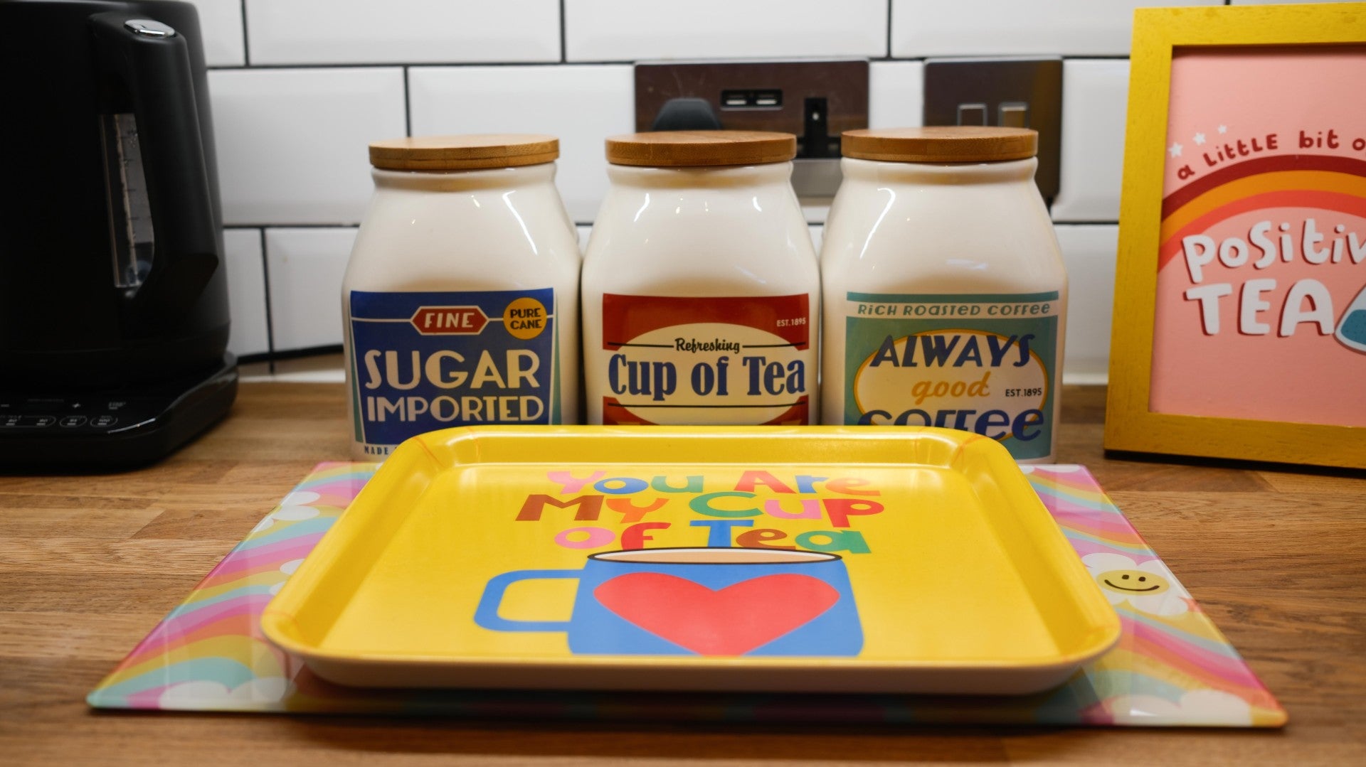 Yellow tray with a colorful design on a kitchen counter with tea canisters in the background.