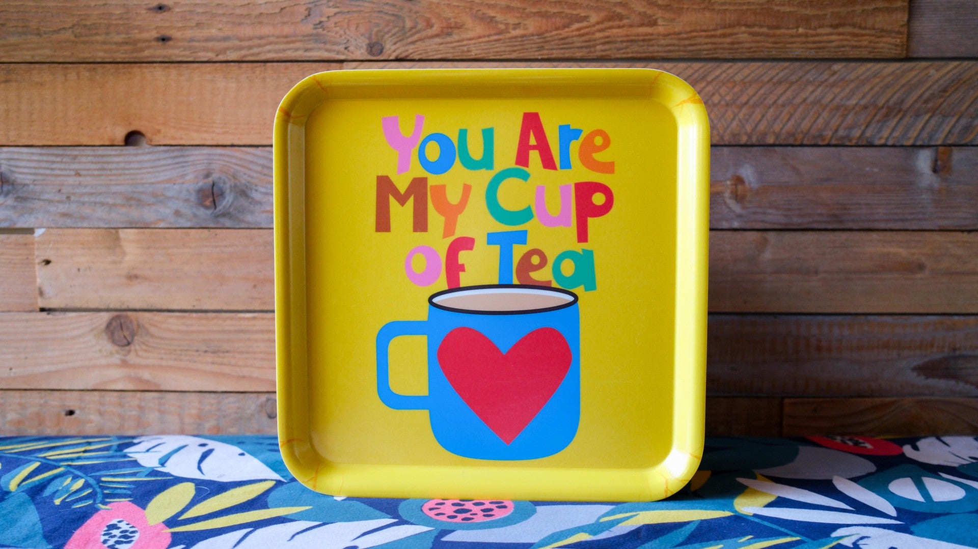 Yellow tray with colorful text and mug design against a wooden background