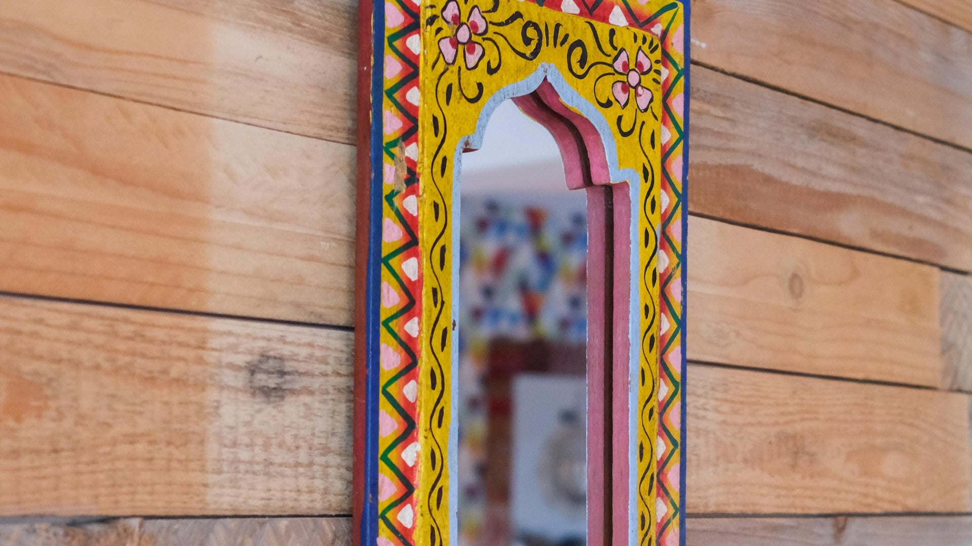 Decorative mirror with colorful frame on a wooden wall