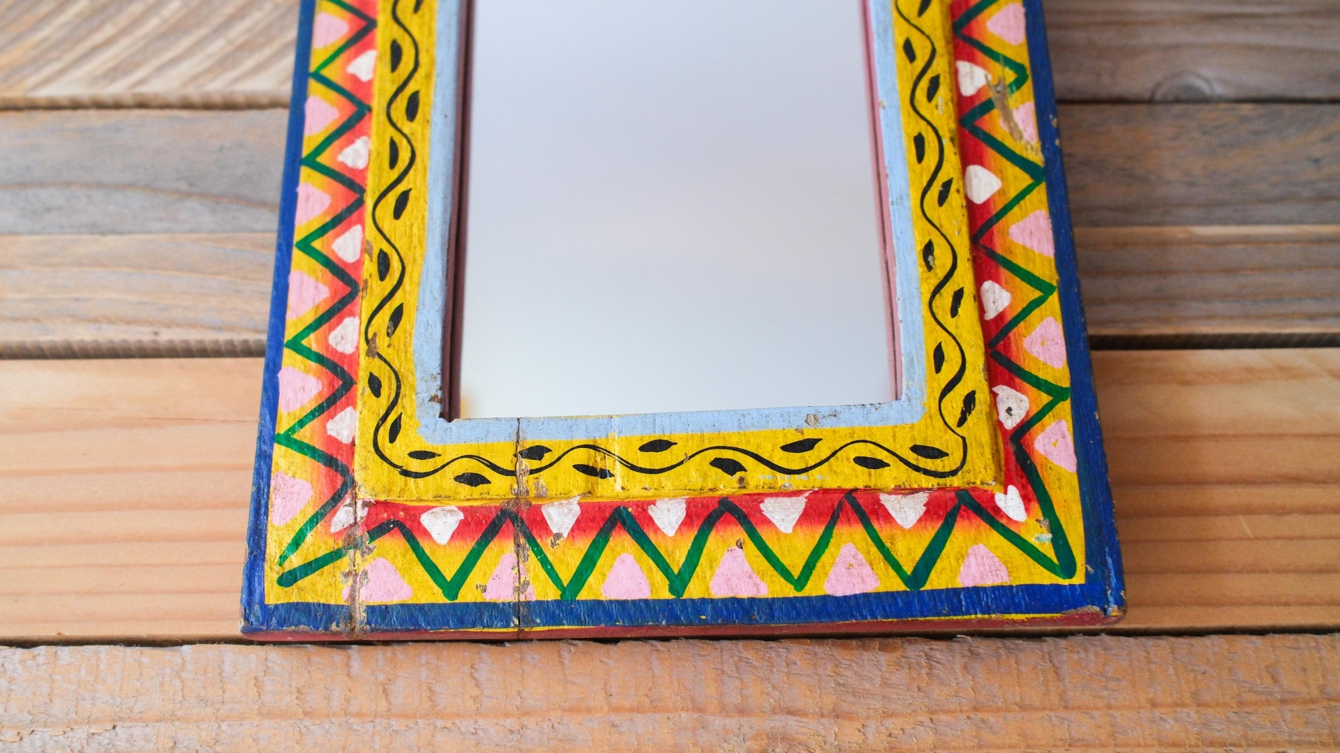 Decorative mirror with a colorful geometric frame on a wooden surface