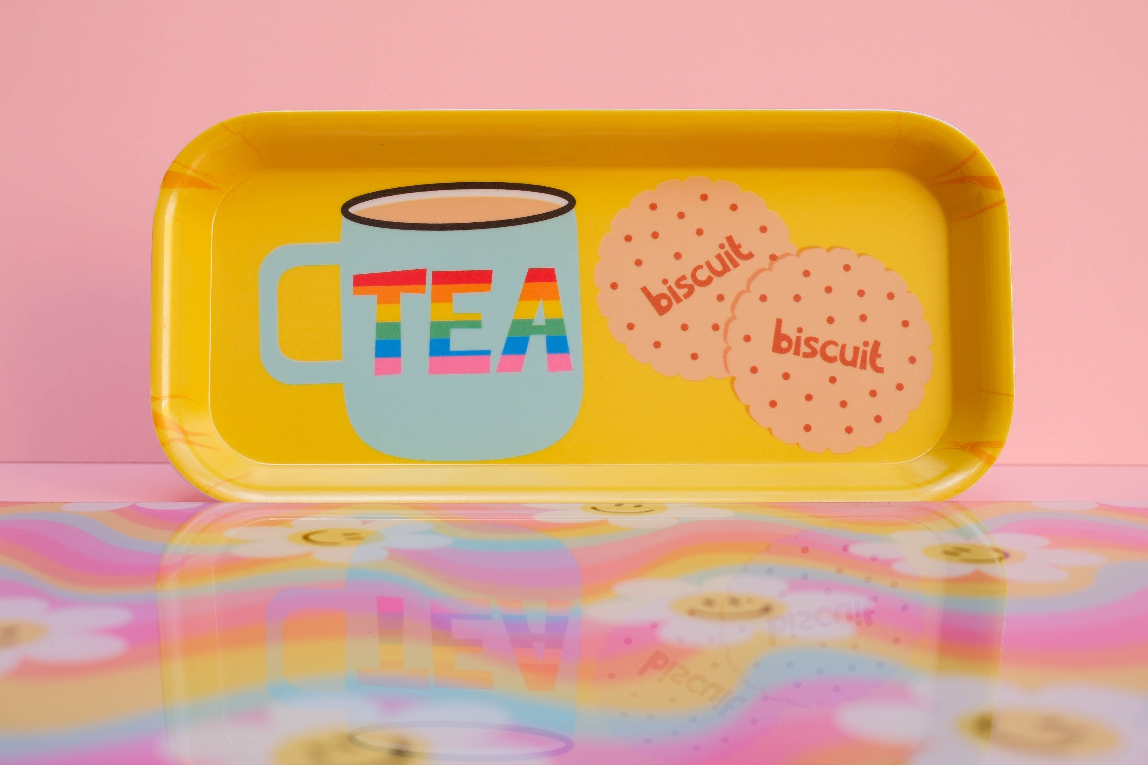 Yellow tea and biscuit tray with a colorful 'TEA' mug and 'biscuit' cookies on a pink and yellow patterned background