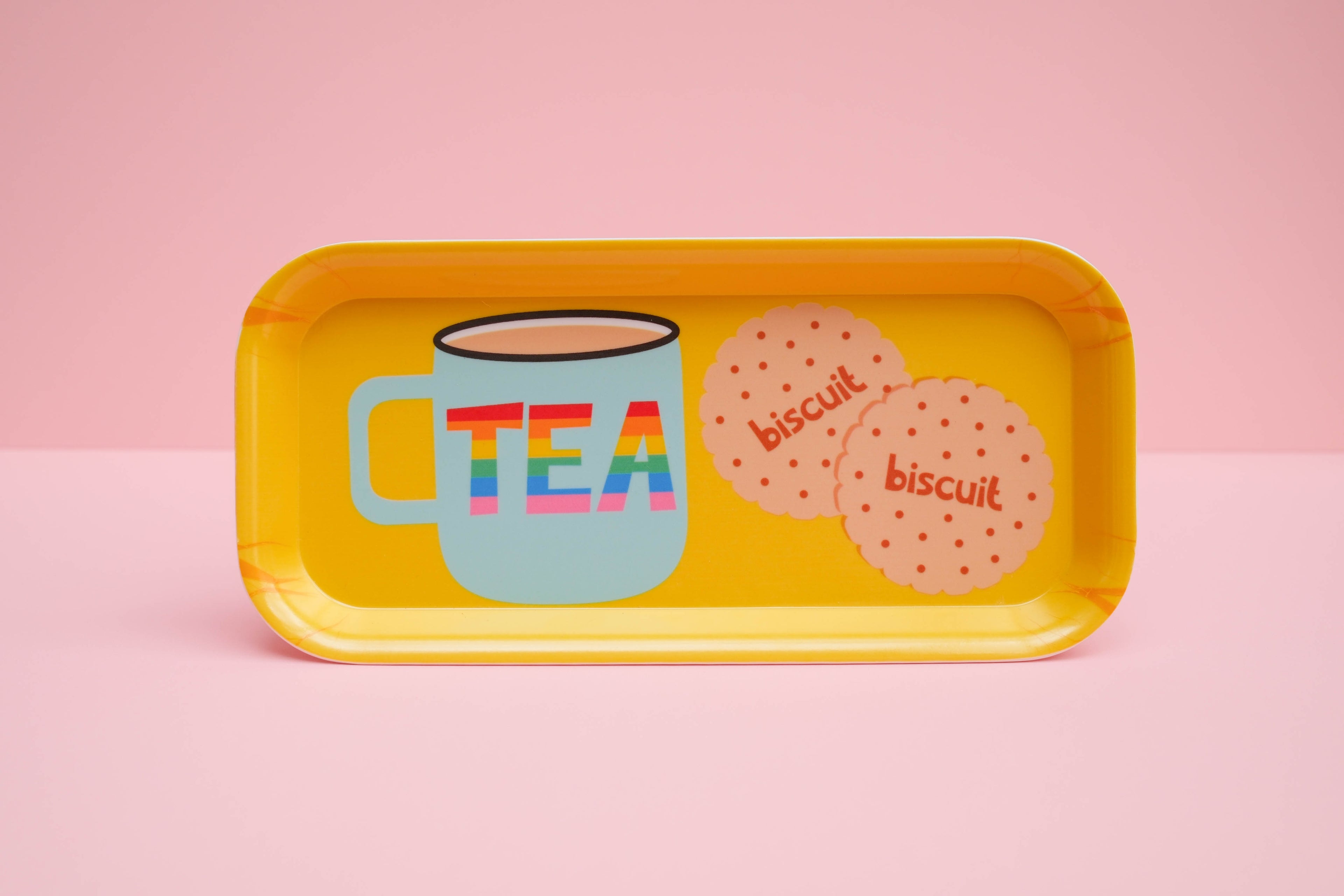 Yellow tray with a mug labeled 'TEA' and two biscuit shapes on a pink background