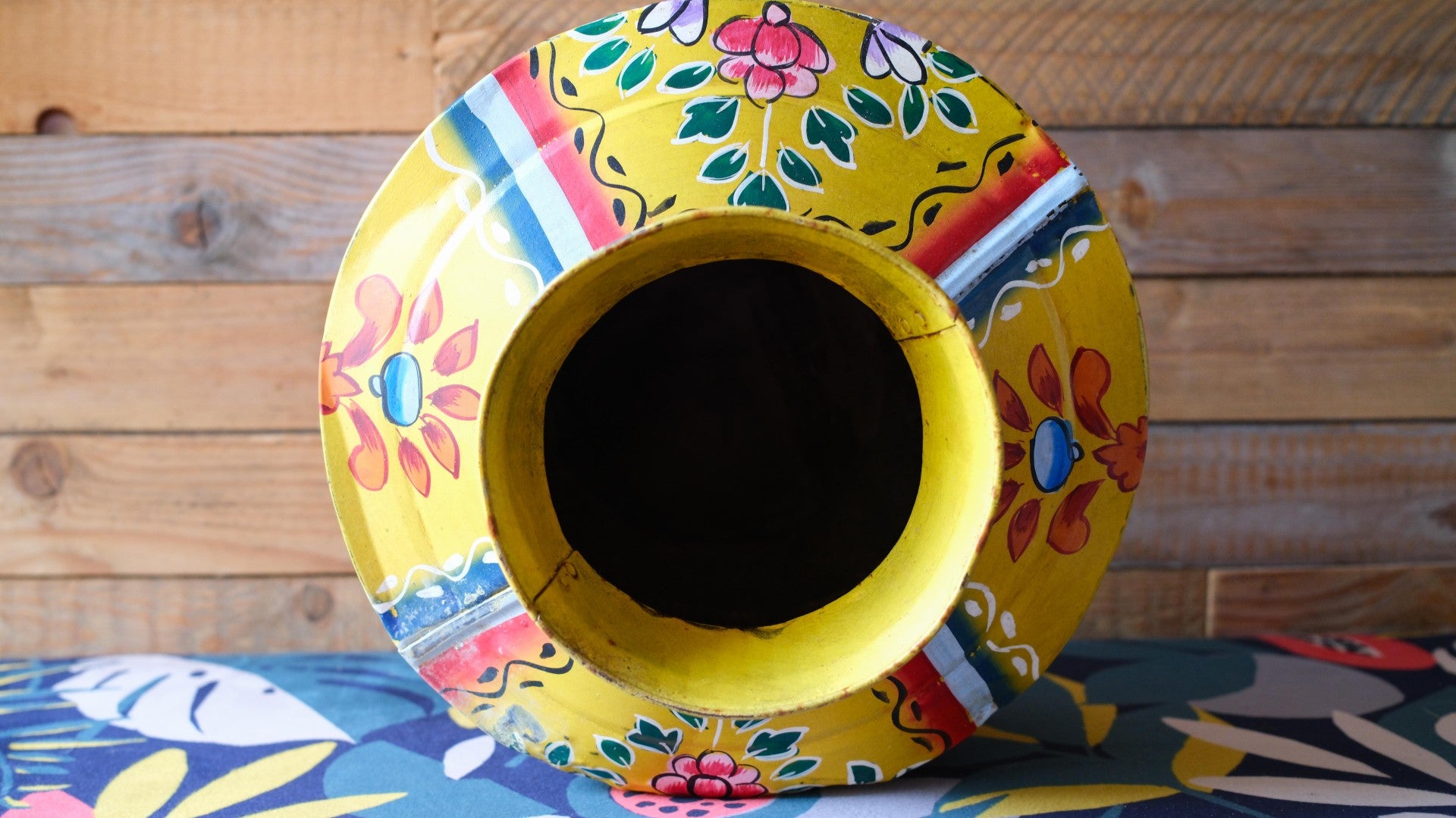 Decorative yellow metal pot with floral patterns on a wooden surface