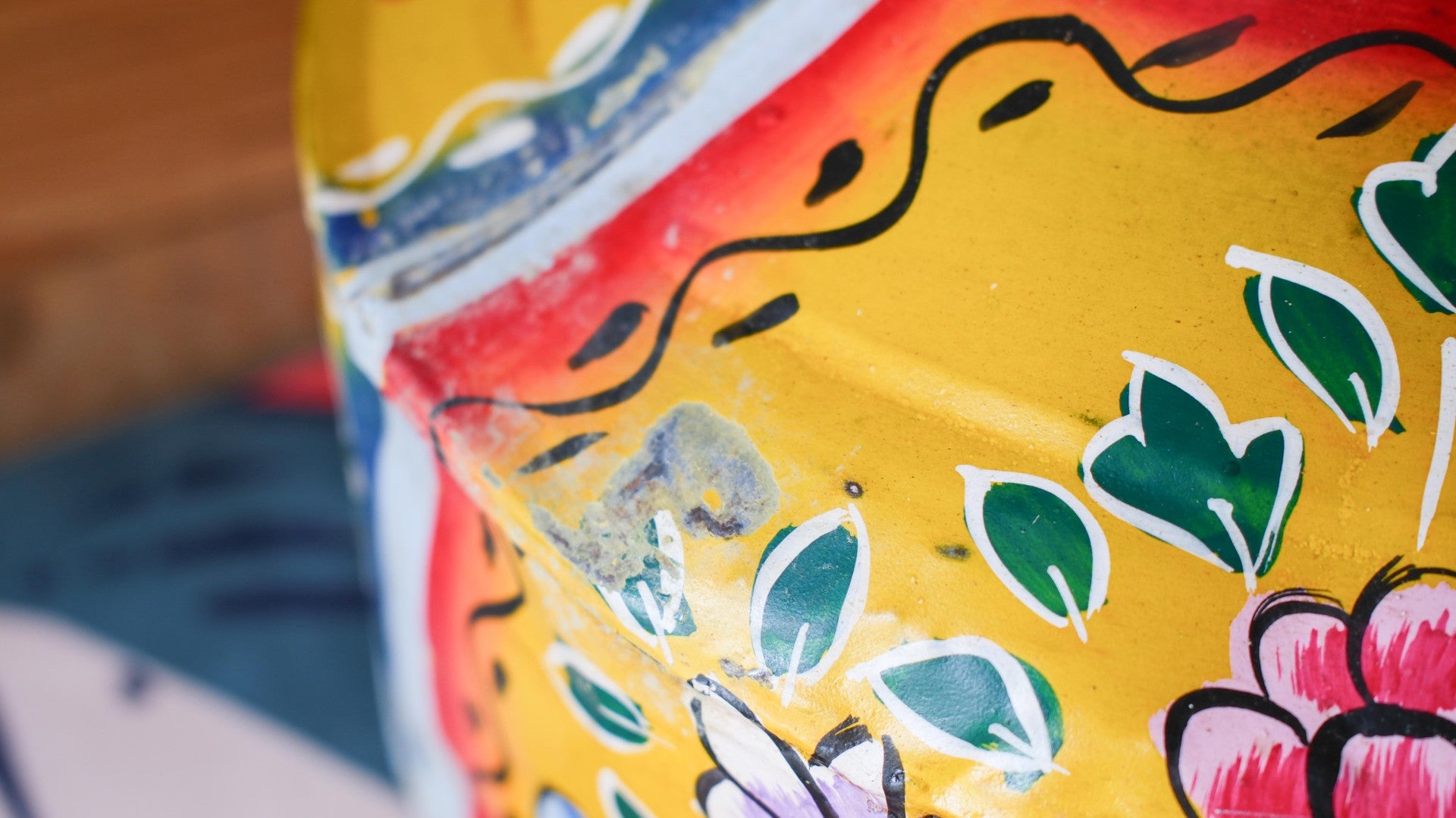 Close-up of a colorful metal pot with floral patterns on a blurred background